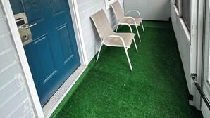 A covered porch with artificial grass, a blue door, and two white chairs. - Pilgrim Inn & Cottages (Plymouth)