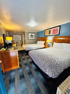 A hotel room with two beds, a desk, a chair, a lamp, and a framed picture on the wall. - Pilgrim Inn & Cottages (Plymouth)