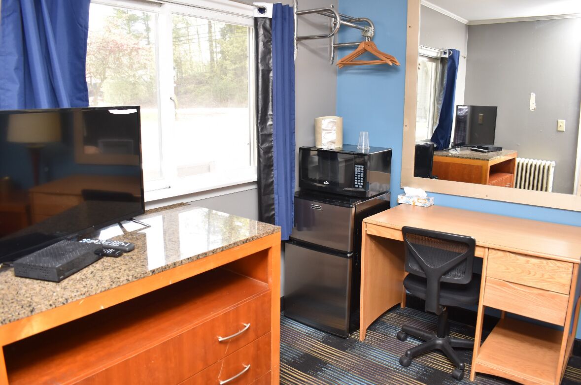 A compact hotel room with a kitchenette, a wooden desk, a chair, a television, a microwave, and a refrigerator.