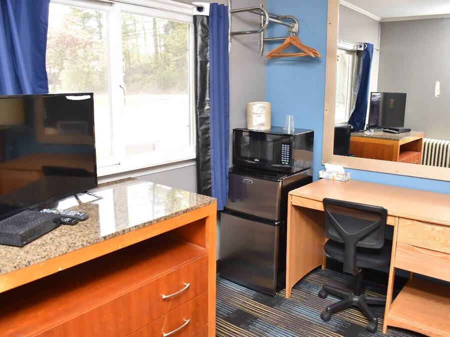 A compact hotel room with a kitchenette, a wooden desk, a chair, a television, a microwave, and a refrigerator.