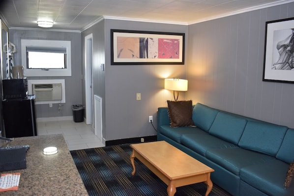 A living room with a teal sofa, a wooden coffee table, a lamp, and a framed abstract painting on the wall. - Pilgrim Inn & Cottages (Plymouth)