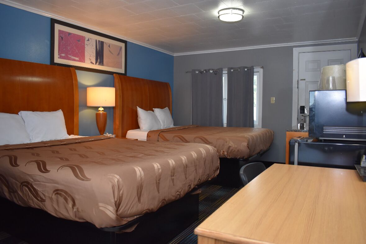 A hotel room with two beds, a desk, a television, and a lamp.