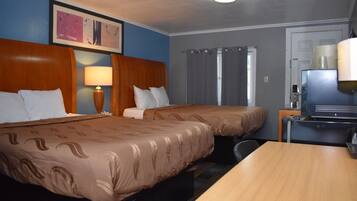 A hotel room with two beds, a desk, a television, and a lamp.