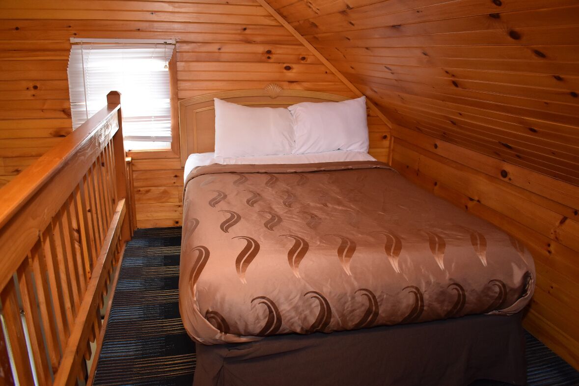 A wooden cabin room with a bed, a window, and a wooden railing.
