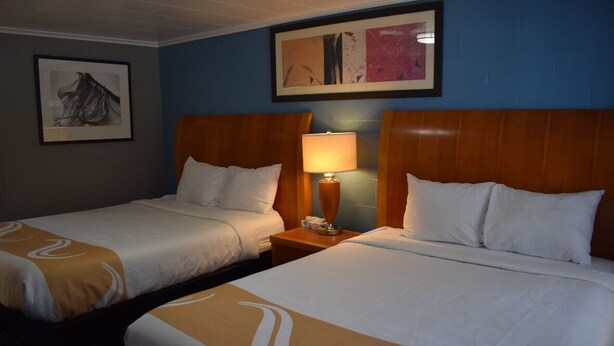 A hotel room with two single beds, a nightstand with a lamp, and artwork on the walls. - Pilgrim Inn & Cottages (Plymouth)