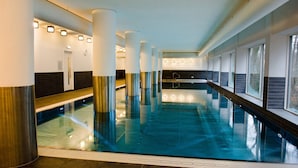 Une piscine intérieure moderne avec des parois en verre transparent, un sol carrelé et un banc le long du bord.