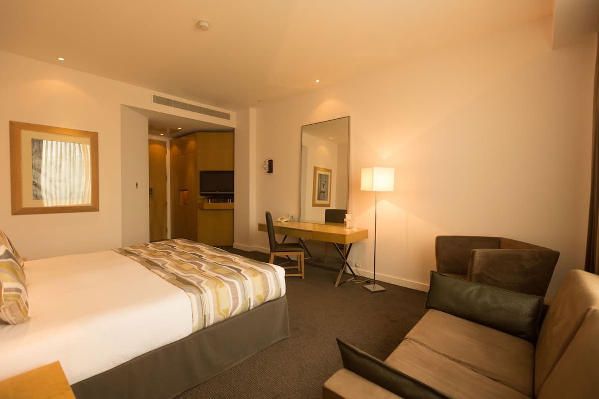 Quarto de hotel com cama, escrivaninha, cadeira e sofá.