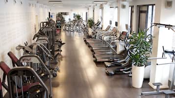 Un gimnasio con cintas de correr, elípticas y máquinas de pesas dispuestas en filas.