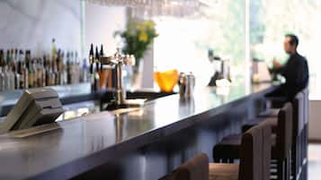 A bar area with a counter, bar stools, a cash register, and a variety of bottles in the background.