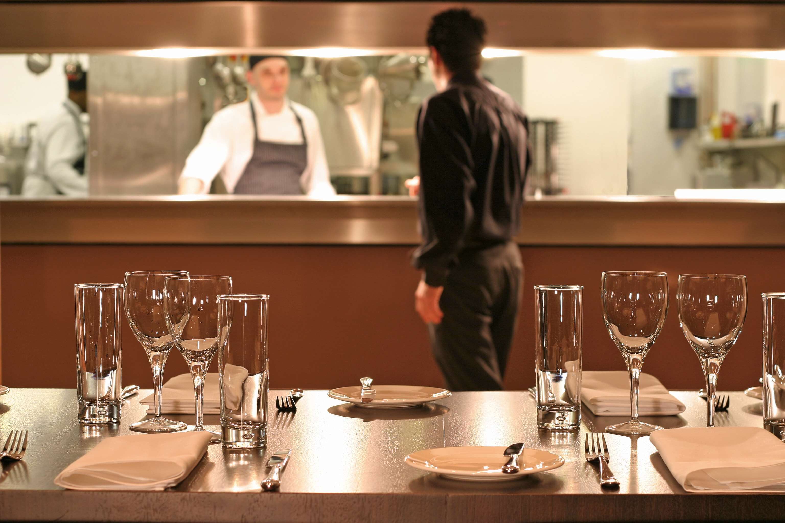 A restaurant setting with a table set for two, complete with wine glasses, plates, and cutlery.