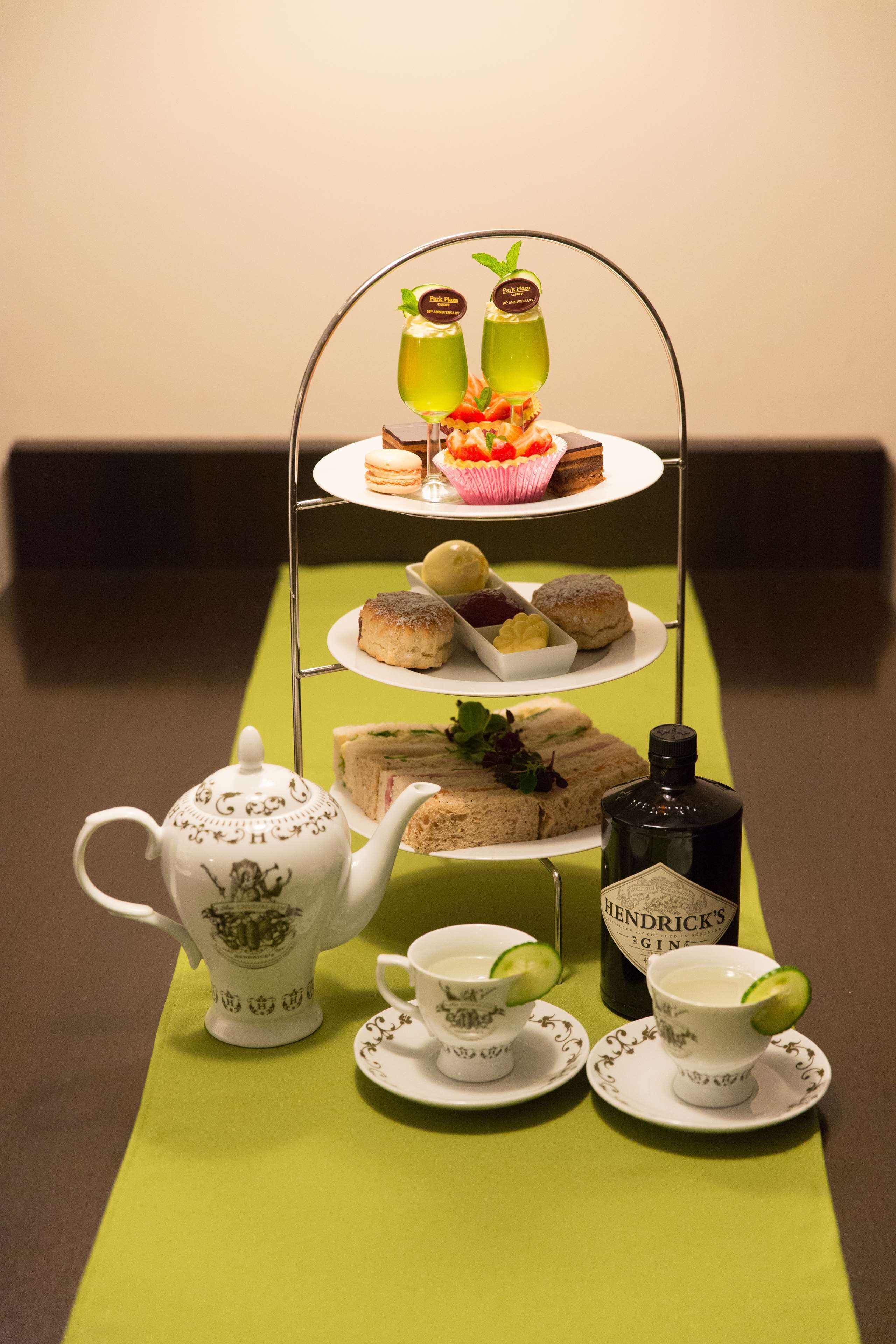 Servicio de té con tetera, tazas, una botella de ginebra Hendrick's y un bandejón de sándwiches y pasteles.