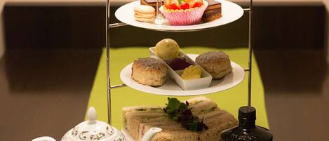 Servicio de té con tetera, tazas, una botella de ginebra Hendrick's y un bandejón de sándwiches y pasteles.