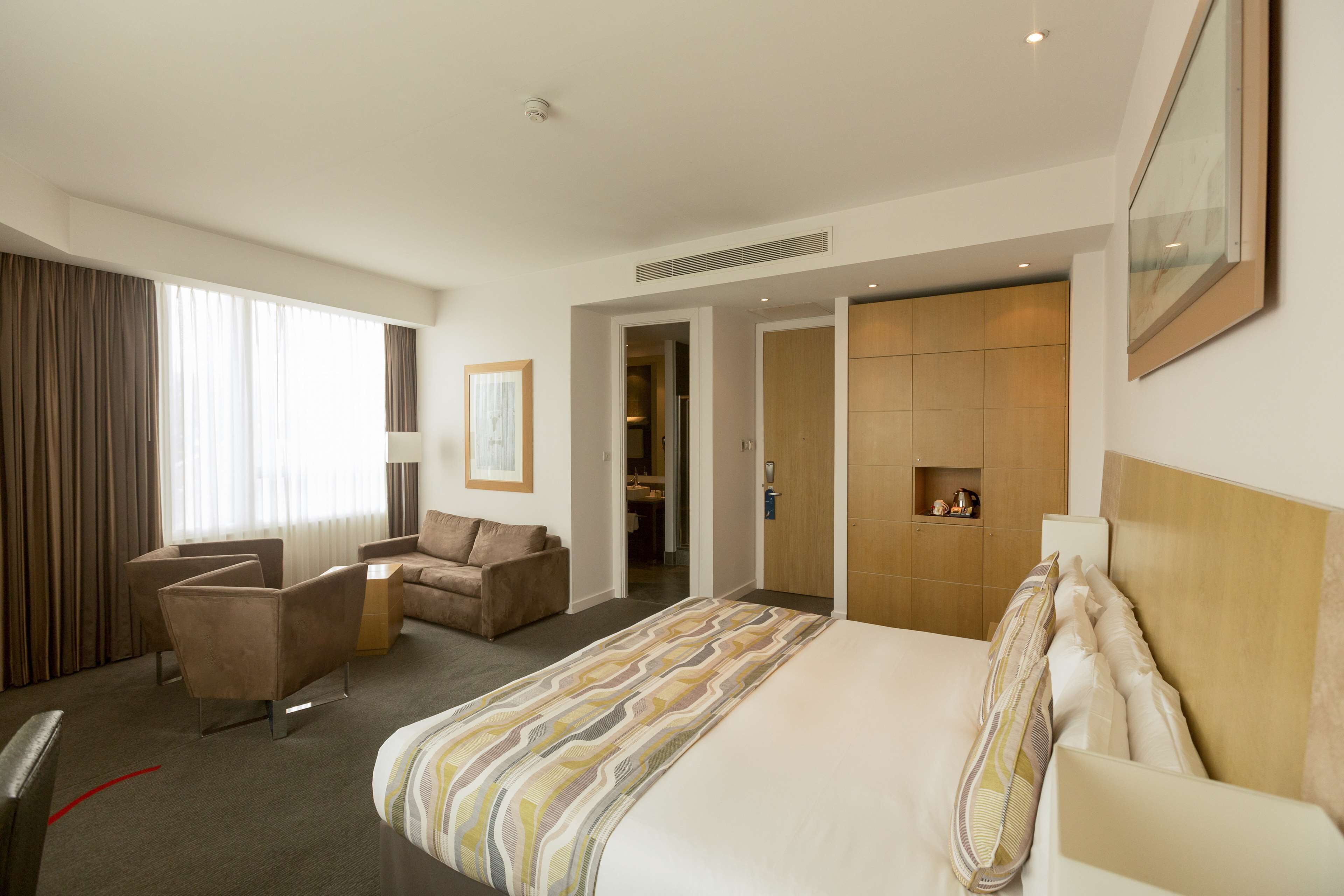 A hotel room with a bed, a sofa, a chair, and a desk. There is a door leading to a bathroom and a closet.