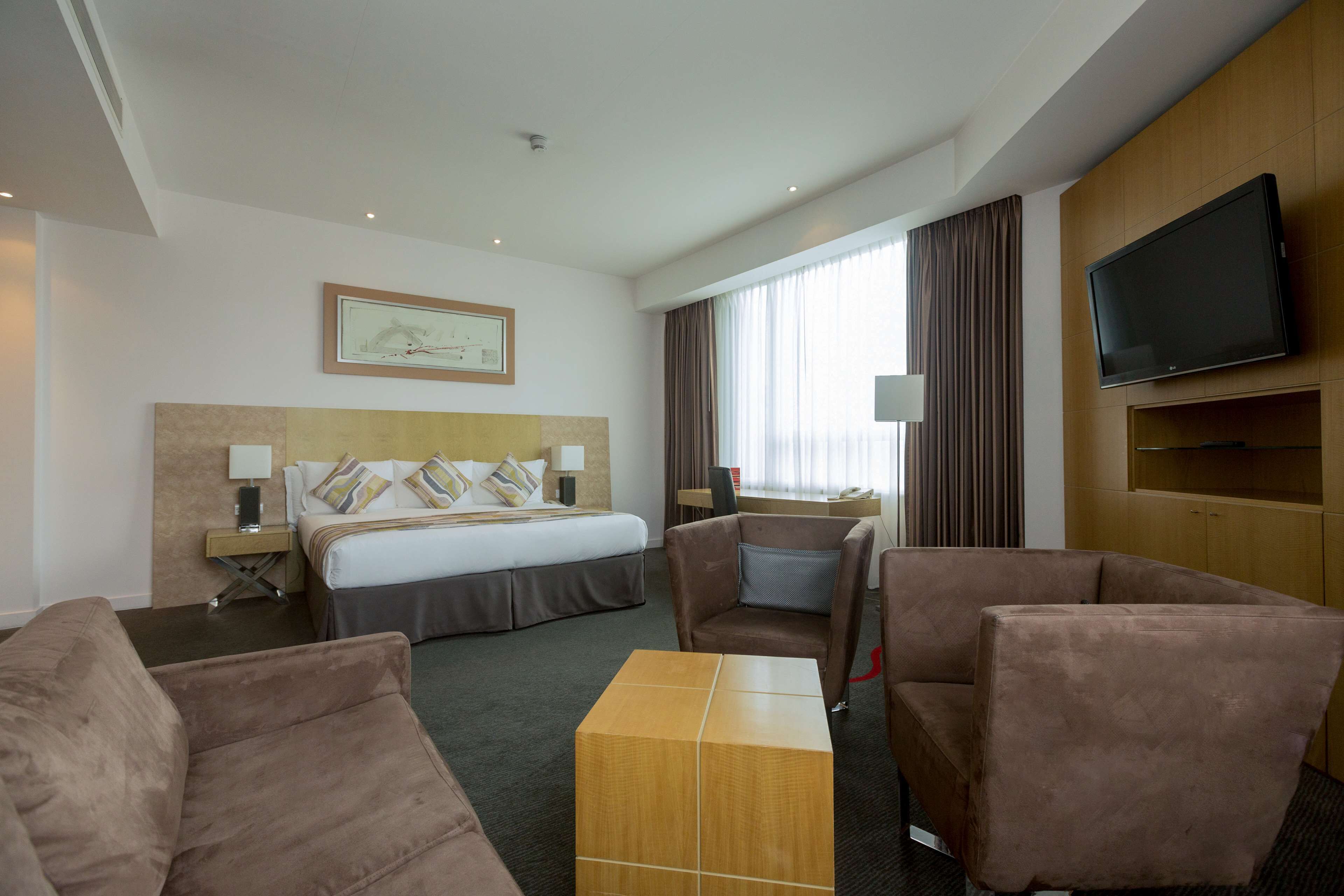 A hotel room with a bed, a TV, a desk, and two sofas.