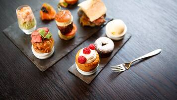 A variety of desserts on a slate board, including a cupcake with raspberries, a slice of cake, and a dessert with a cherry on top.