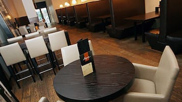A modern restaurant with round tables and cushioned chairs, wooden flooring, and pendant lighting.