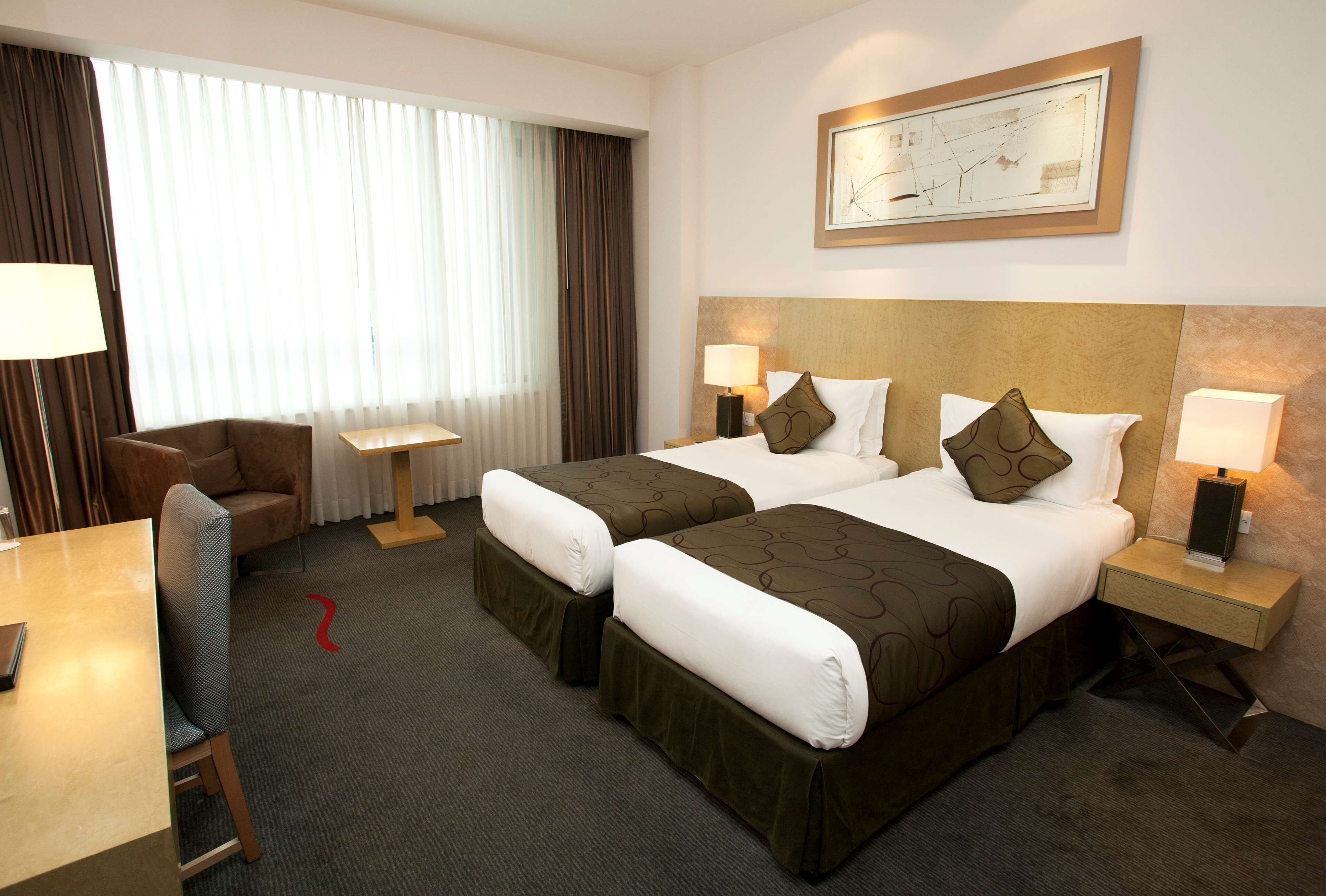 A hotel room with two beds, a desk, a chair, and a large window with curtains.