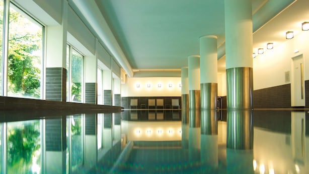 Une piscine intérieure moderne aux parois en verre transparent, qui laisse entrer la lumière naturelle et illumine l’espace.