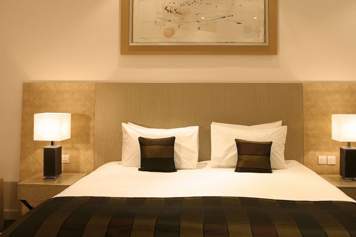 Quarto de hotel com uma cama grande, duas luminárias de cabeceira e uma obra de arte emoldurada acima da cama.