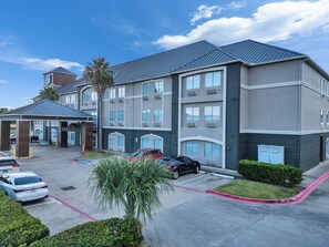 A multi-story hotel with a covered entrance, parking area, and a palm tree. - Platinum Inn & Suites Webster (Webster)