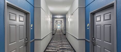 A hotel hallway with a checkered carpet, grey doors, and blue walls.