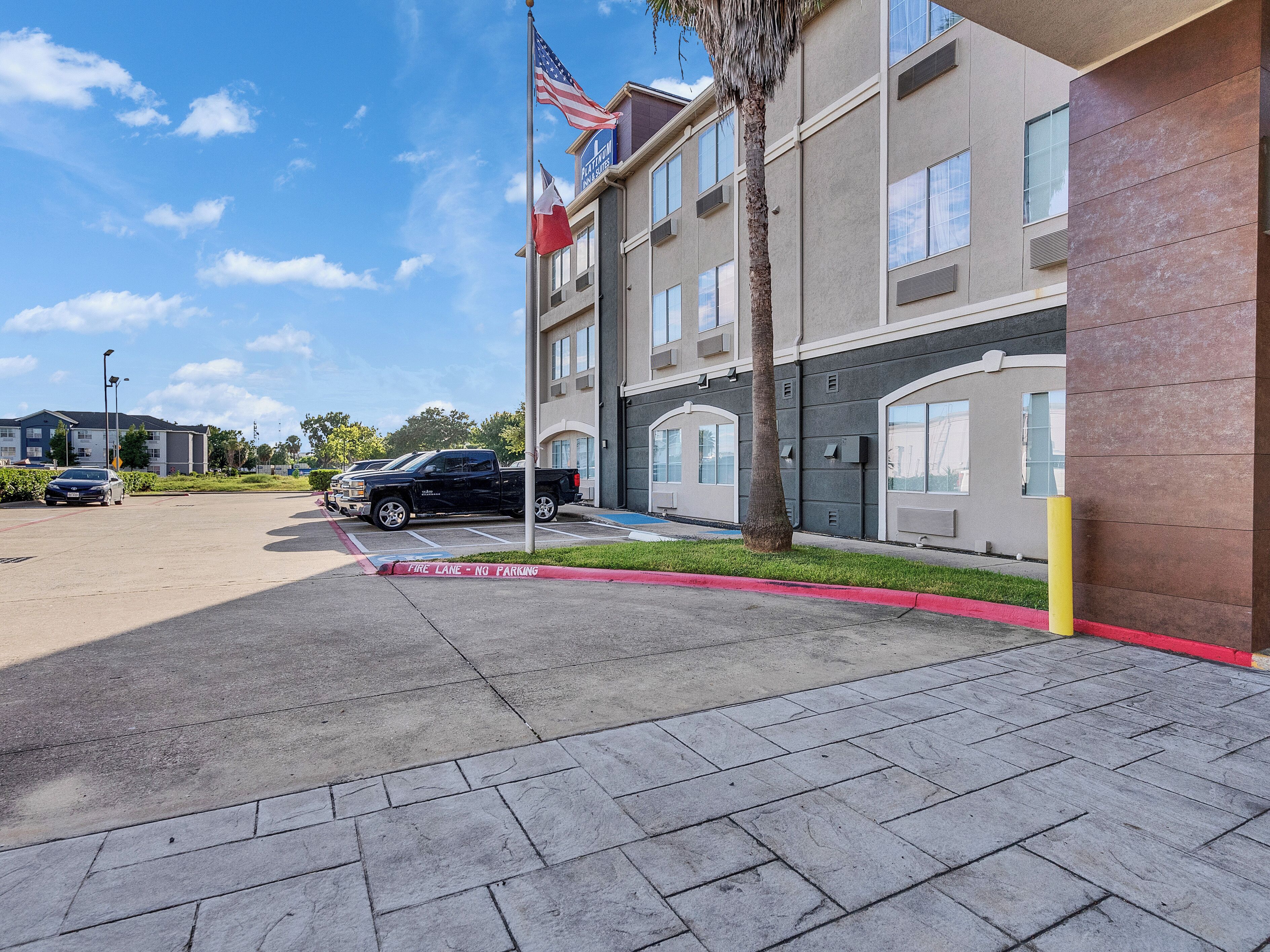 A multi-story hotel with a parking area, a flagpole with the American flag, and a palm tree.