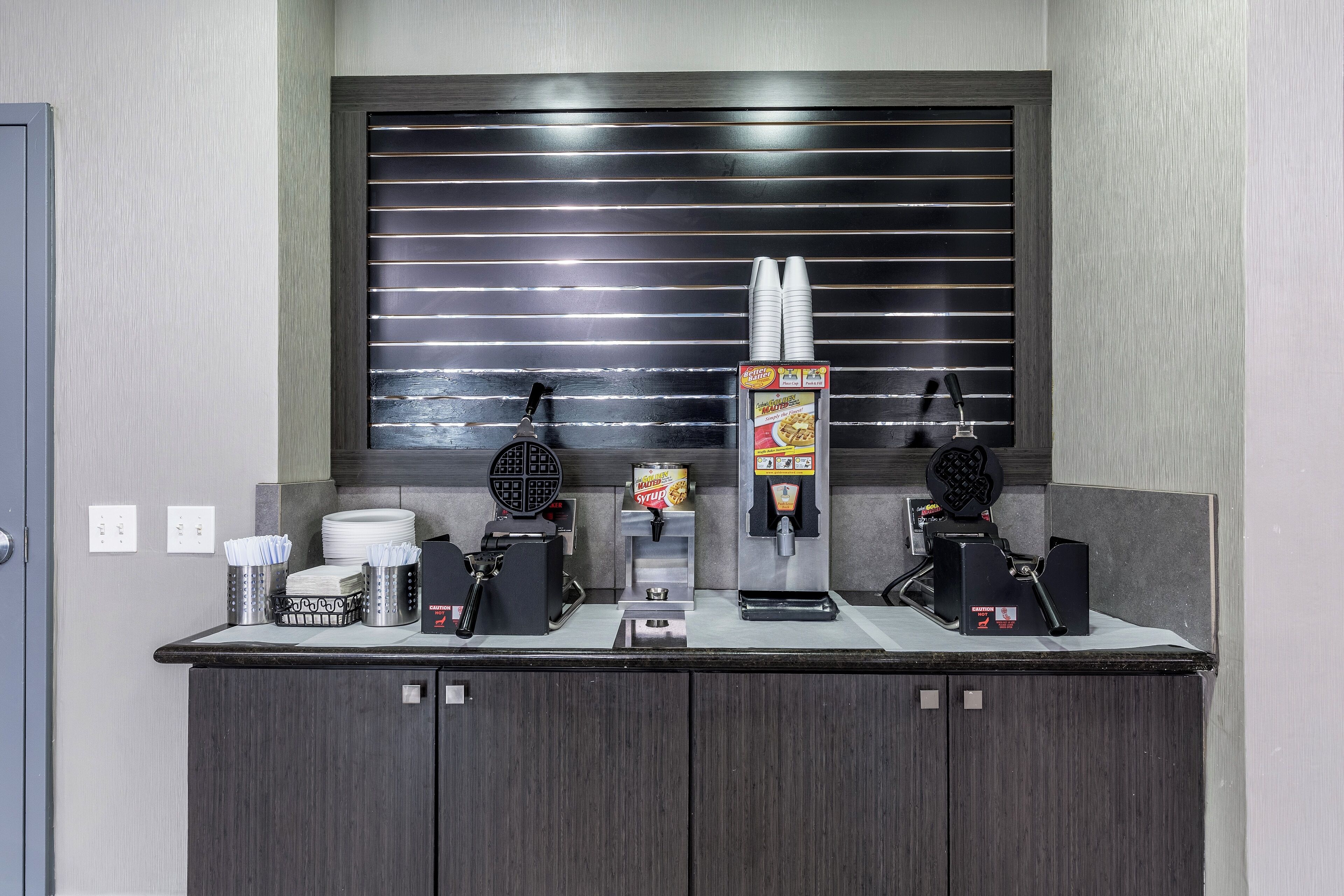 A self-service beverage station with a waffle maker, coffee machine, and a soda dispenser.
