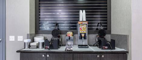 A self-service beverage station with a waffle maker, coffee machine, and a soda dispenser.