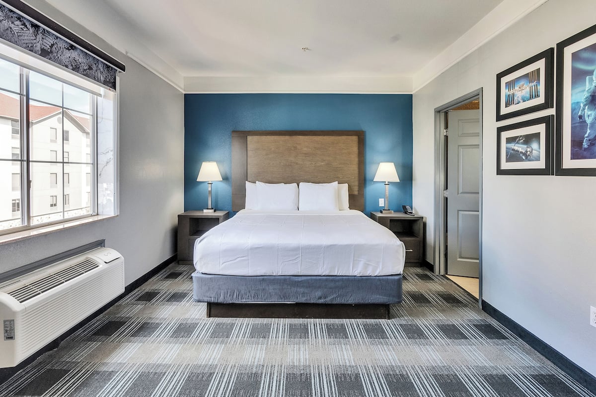Ein Hotelzimmer mit einem großen Bett, zwei Nachttischen inklusive Lampen, einem Fenster und einer Wand-Klimaanlage.