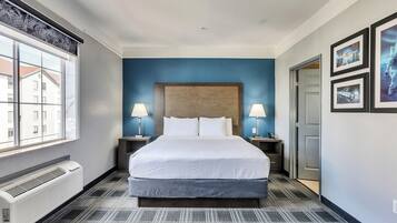 Una habitación de hotel con una cama grande, dos mesitas de noche con lámparas, un ventanal y un aire acondicionado de pared.