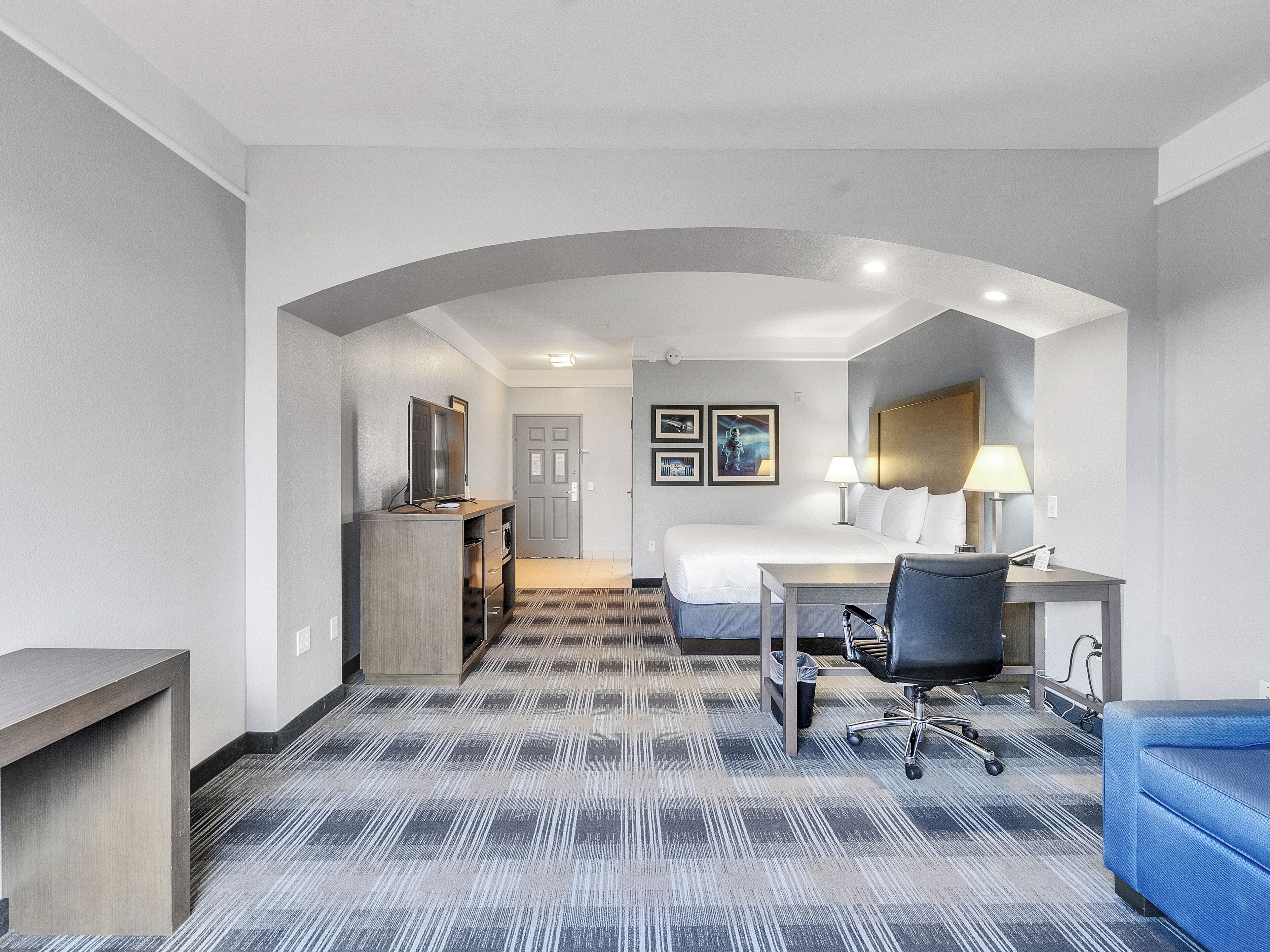 A hotel room with a bed, desk, chair, and a small kitchenette.