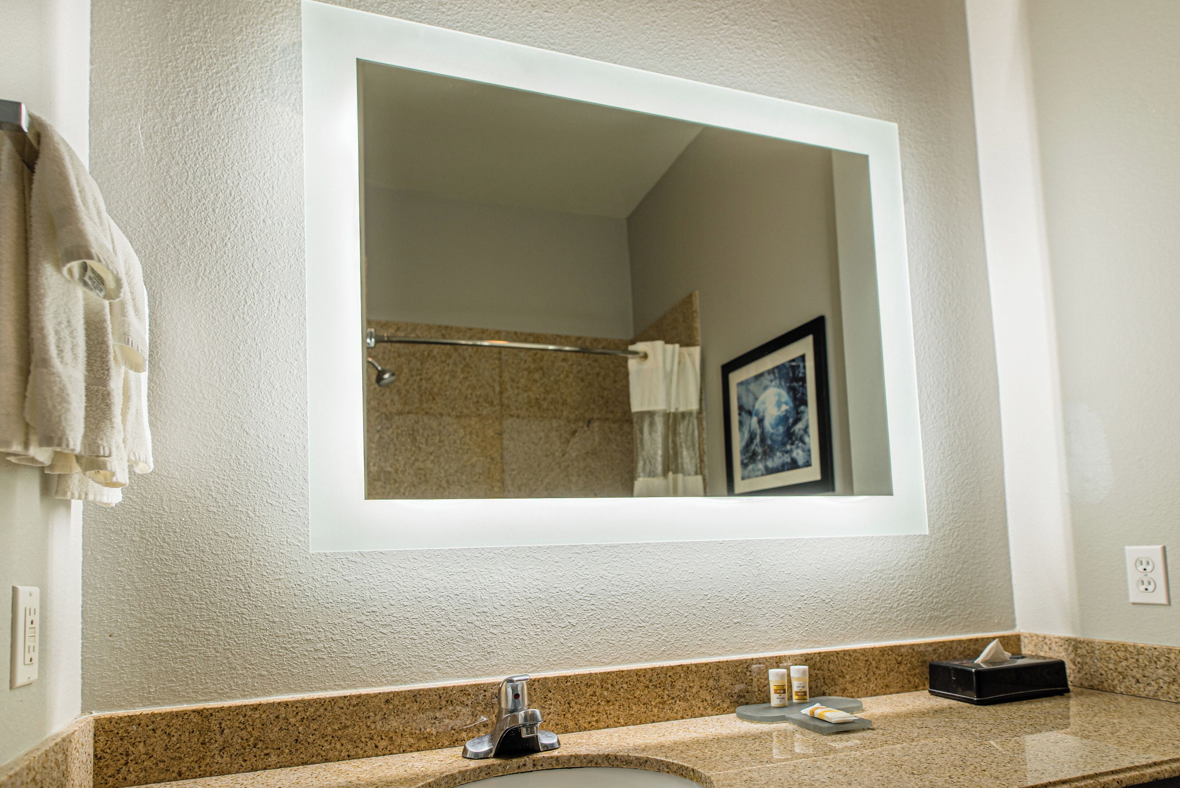Un bagno con uno specchio grande, un ripiano in granito e un portasciugamani.