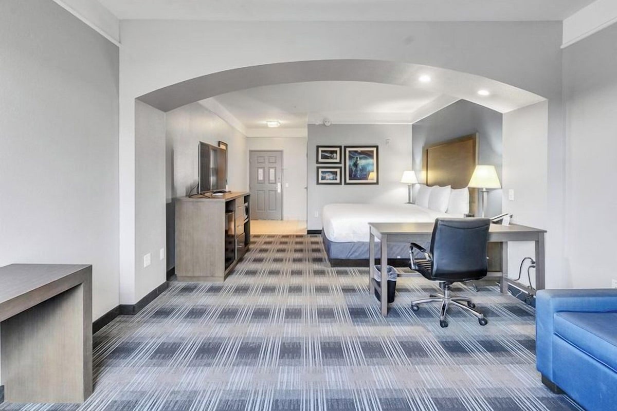 A hotel room with a bed, desk, chair, and a small kitchenette.