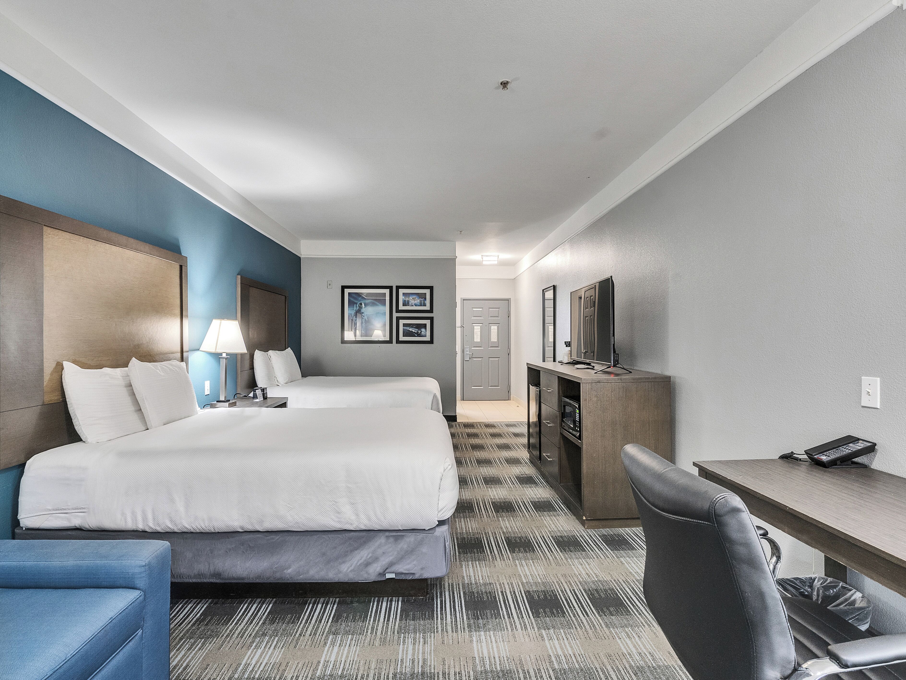 Een hotelkamer met twee bedden, een bureau, een stoel, een televisie en een minibar.