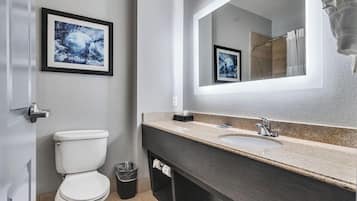 Un baño moderno con inodoro blanco, lavabo con encimera de mármol y un espejo grande.