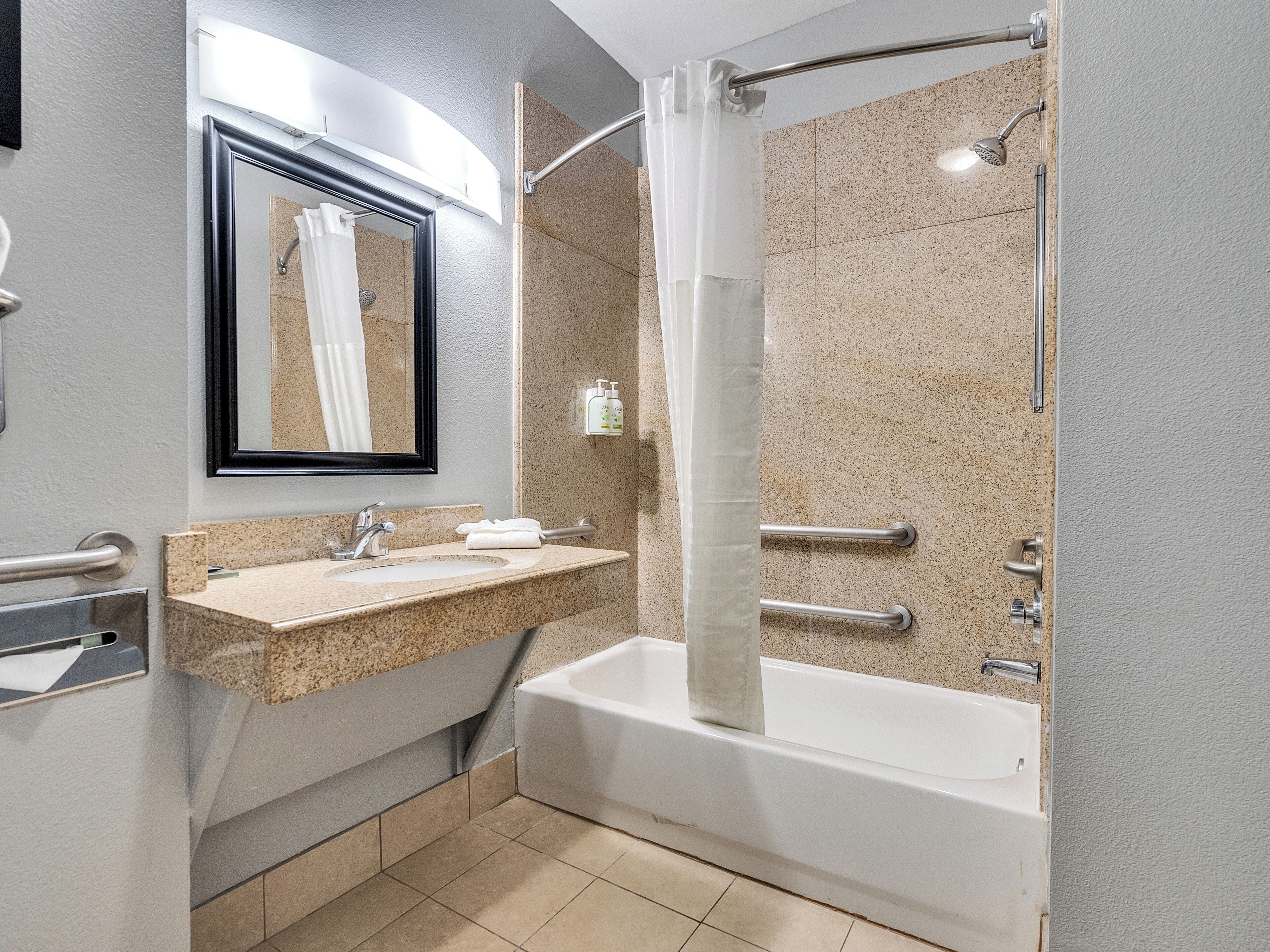 A bathroom with a sink, mirror, shower, and grab bars.