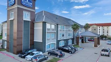 Un hotel con un llamativo letrero de Platinum Inn & Suites, que presenta un diseño arquitectónico moderno con una combinación de fachada de ladrillo y color gris, varios espacios de estacionamiento y una pequeña zona cubierta con la bandera estadounidense.