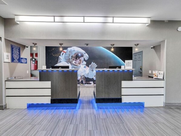 A reception area with a central desk, a large space-themed mural, and a blue-lit pathway leading to the desk. - Platinum Inn & Suites Webster (Webster)
