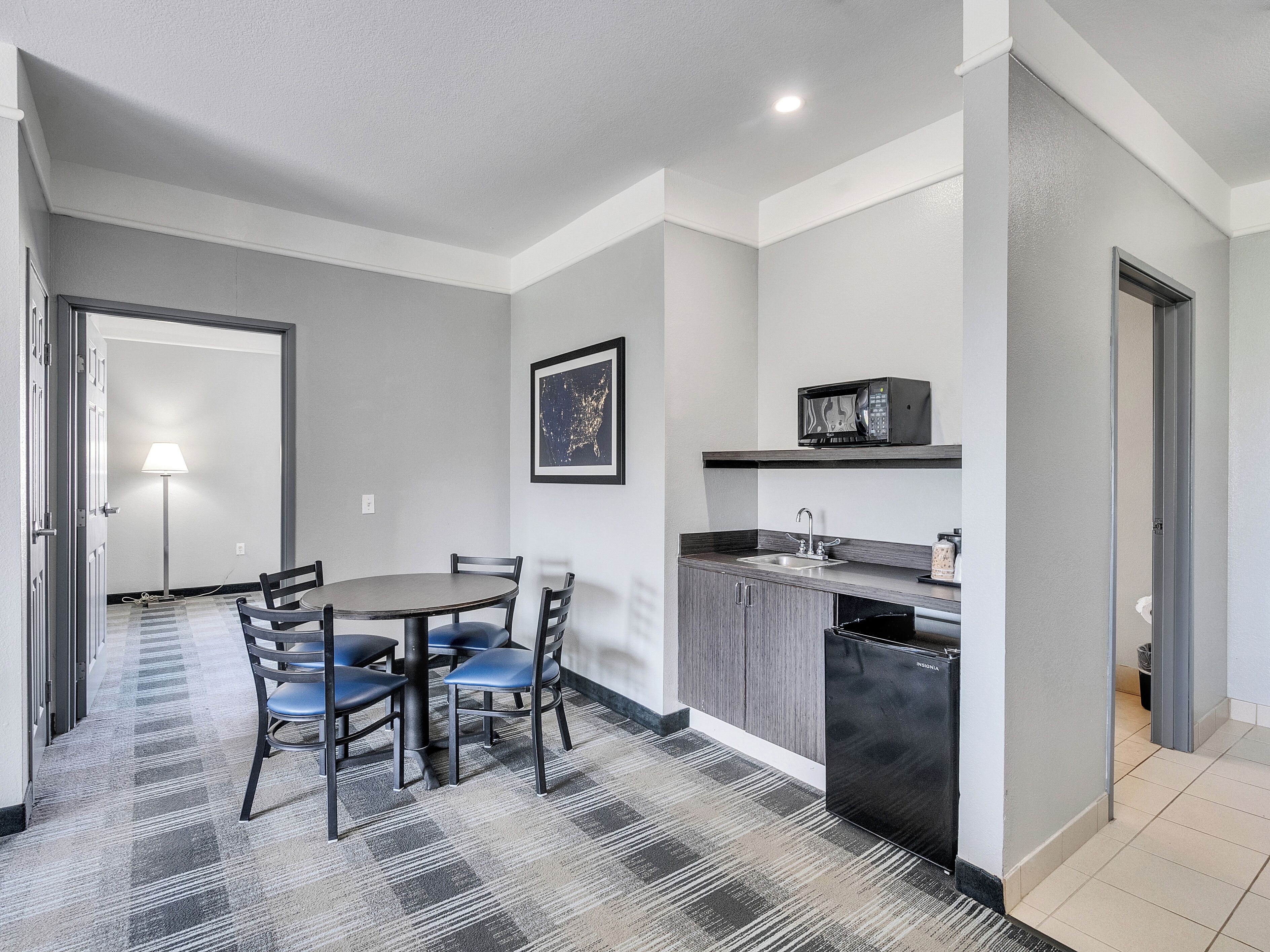 A compact kitchen with a microwave, sink, and a small countertop. There is a dining area with a round table and chairs.