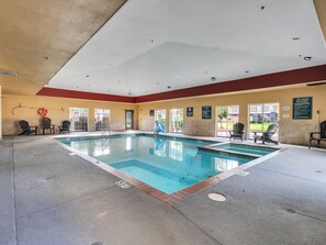 An indoor swimming pool with clear water, surrounded by chairs and a lifebuoy on the wall. - Platinum Inn & Suites Webster (Webster)