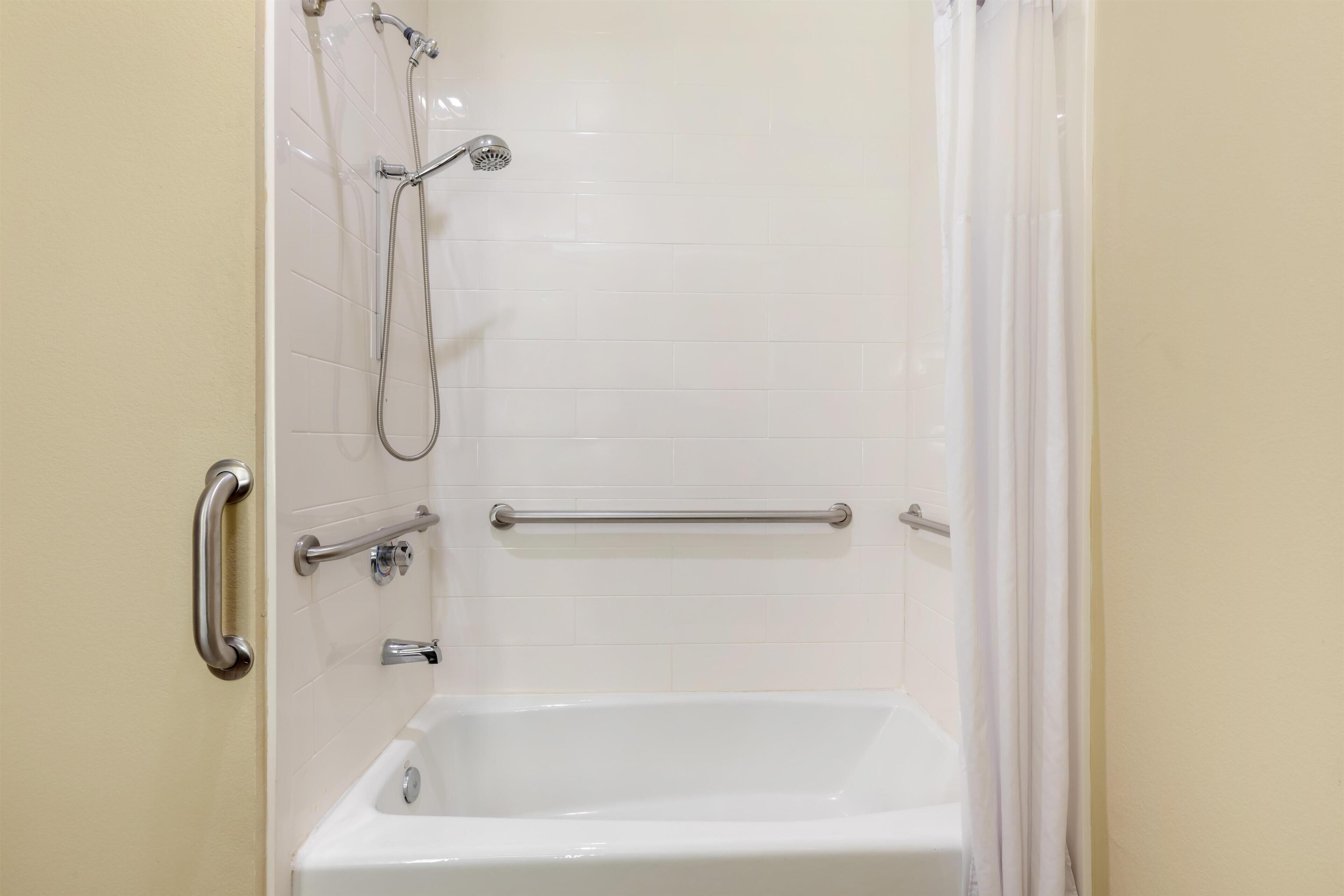 A bathroom with a white bathtub, a showerhead, and grab bars.