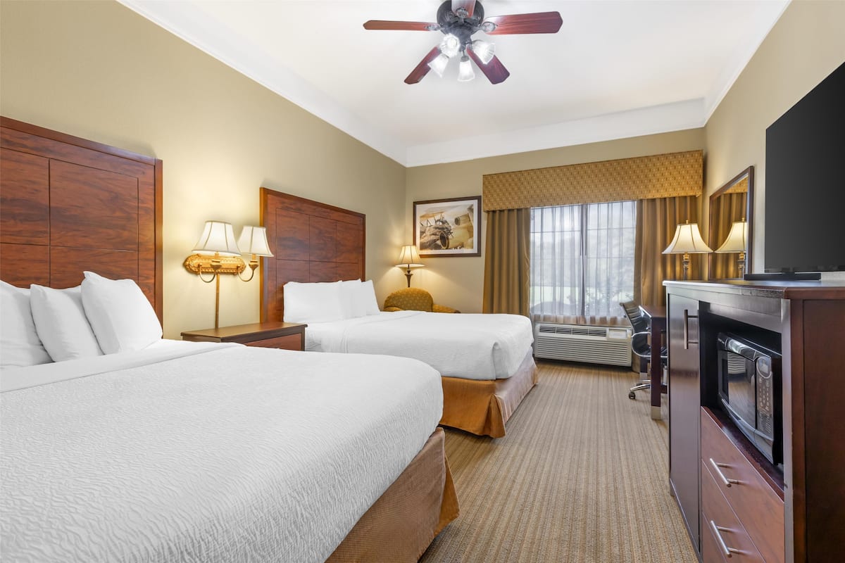 Une chambre d’hôtel avec deux lits, un ventilateur de plafond, une télévision, un bureau et une fenêtre avec des rideaux.