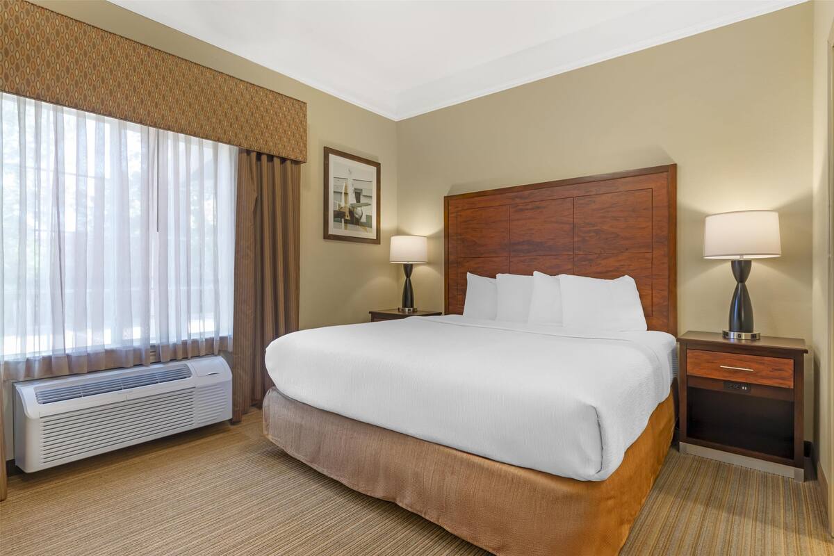Une chambre d’hôtel avec un grand lit, deux tables de chevet avec des lampes, un climatiseur fixé au mur et une fenêtre avec des rideaux.