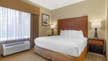A hotel room with a large bed, two bedside tables with lamps, a wall-mounted air conditioner, and a window with curtains.