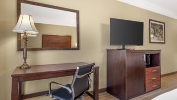 A hotel room with a wooden desk, a chair, a television, a mirror, and a cabinet.