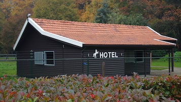 Ein kleines, dunkles Holzgebäude mit rotem Dach, das als Hotel ausgeschildert ist, umgeben von einem Zaun und Herbstlaub.