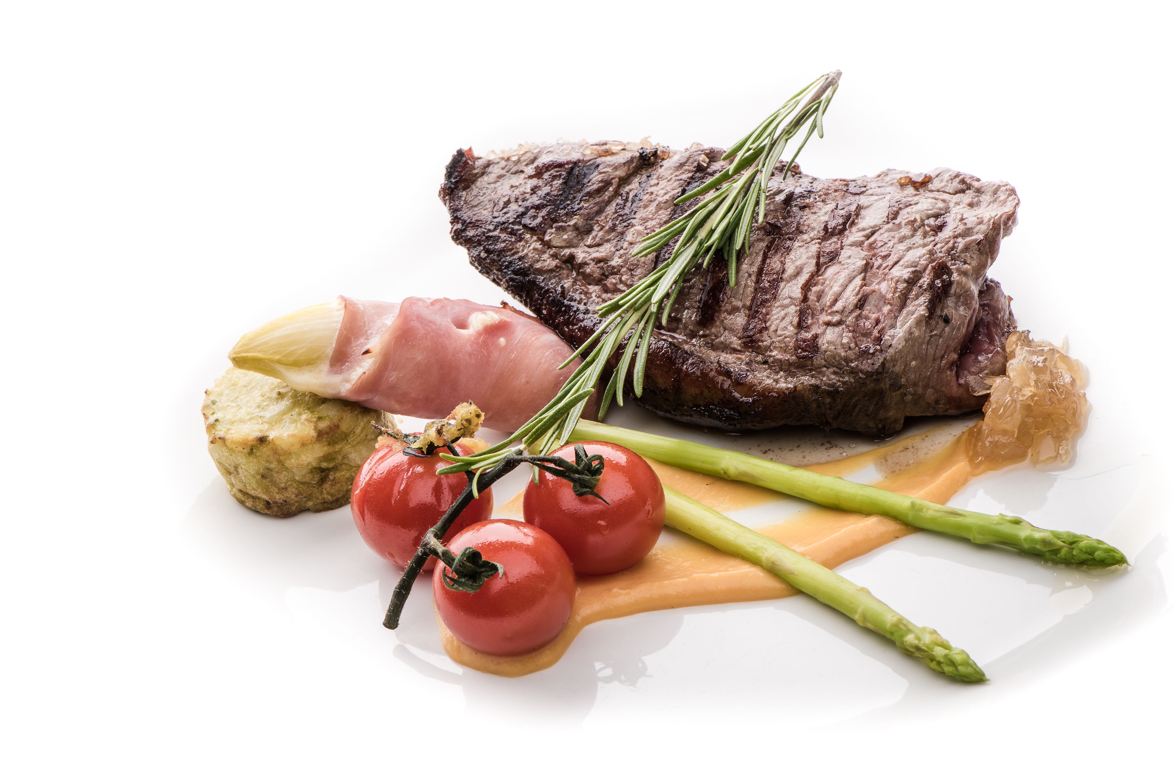 Un plato blanco con carne, espárragos, tomates y salsa.