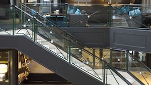 A modern hotel lobby with a glass staircase, seating area with purple upholstered chairs, and a decorative deer head on the wall. - Van der Valk Hotel Gilze - Tilburg (Gilze)