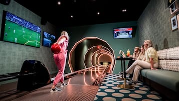 A bowling alley with a neon-lit design, a large screen displaying a sports event, and a seating area with a patterned floor.