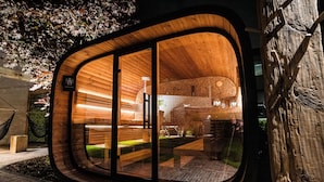 A modern, wooden structure with a curved entrance, a bench inside, and a stone wall with a circular pattern. - Van der Valk Hotel Gilze - Tilburg (Gilze)